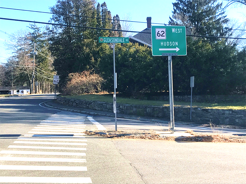 Figure 15 - View across Gleasondale Road (Route 62) of Southeast Intersection Corner. Image shows crosswalk passing to the left of a median to a tall curb and narrow sidewalk made of pavement.